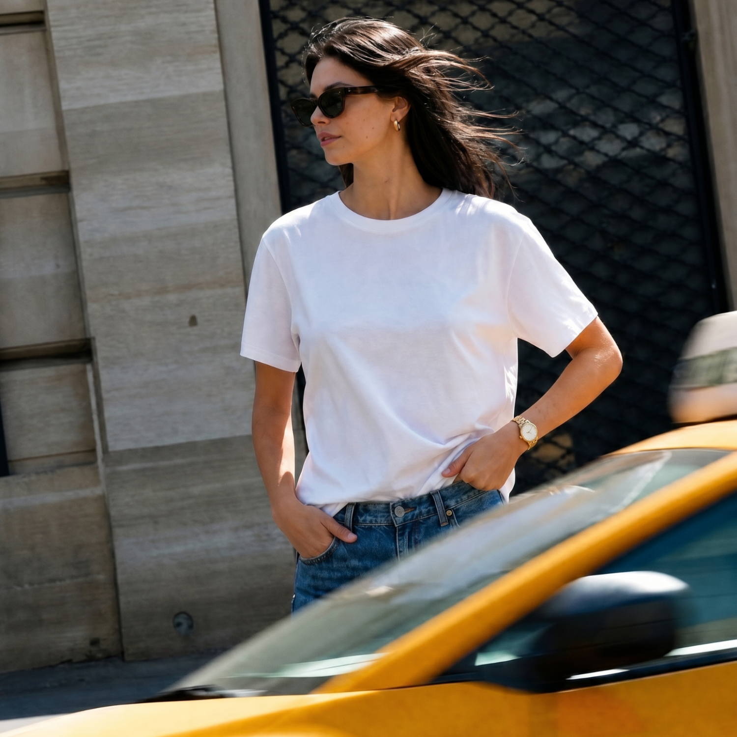 Woman wearing a white t-shirt and sunglasses standing next to a yellow taxi.